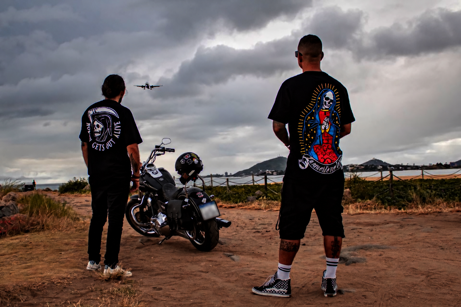 Dois modelos vestindo camisetas Bones junto a uma moto à beira-mar